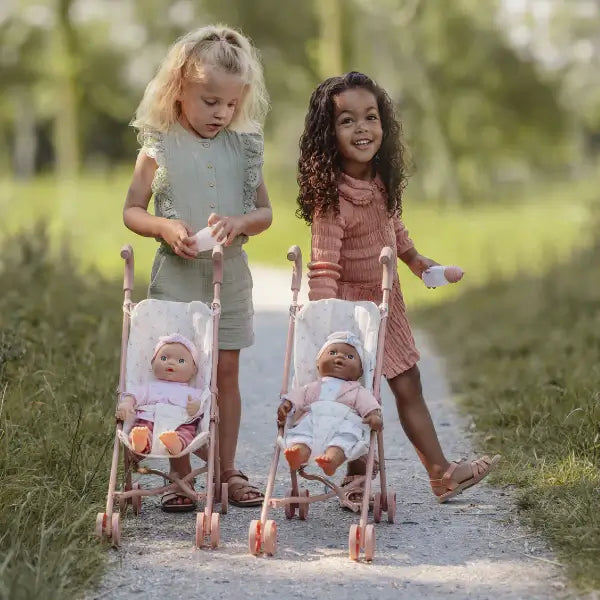 Two children joyfully pushing Little Dutch doll strollers along a sunny path, ready for adventure with their dolls.