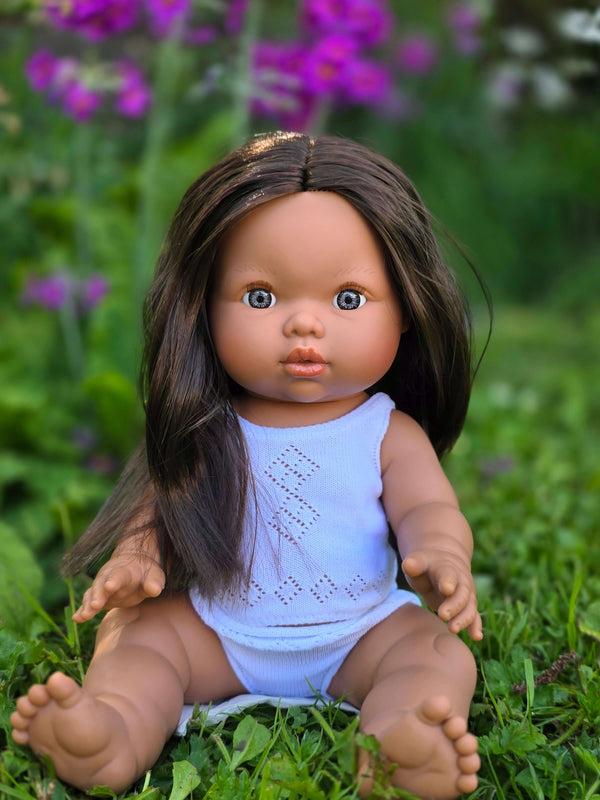 Mini Colettos, Isabel (Hispanic Girl, Brown Straight Hair and Blue Eyes) sitting in grass with flowers.