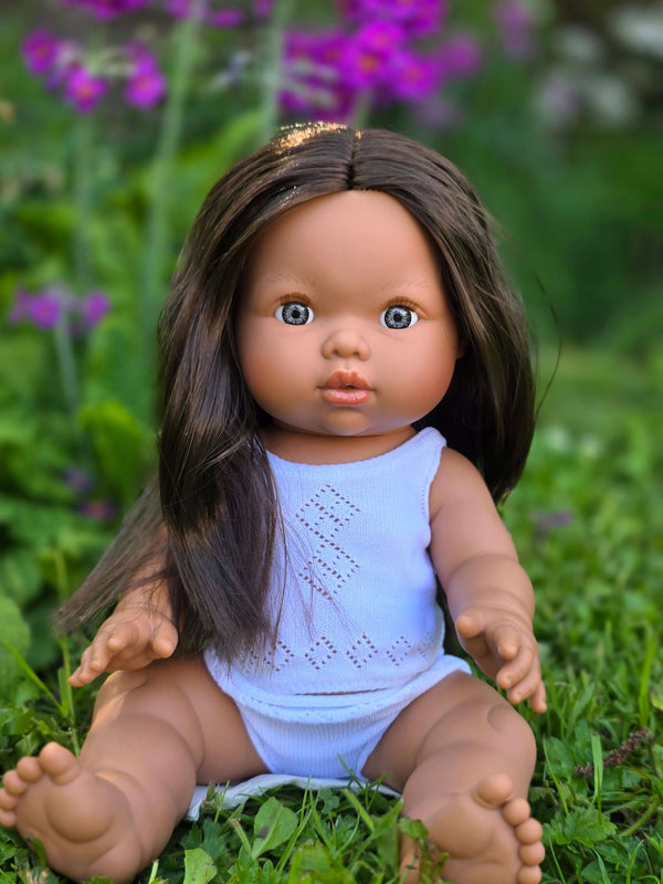 Mini Colettos, Isabel (Hispanic Girl, Brown Straight Hair and Blue Eyes) sitting outdoors in a vibrant garden.