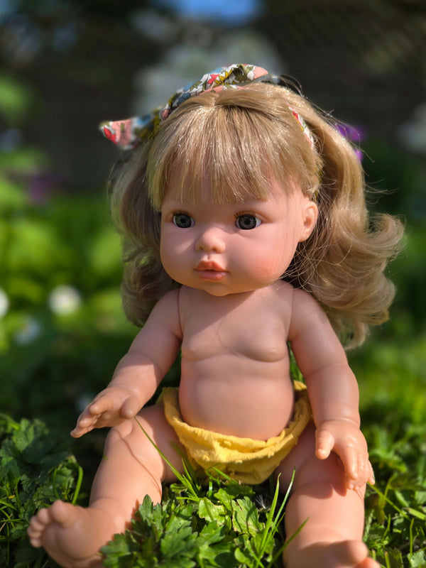 Mini Colettos doll Kate sitting in grass with blonde hair, blue eyes, and floral headband, showcasing her playful charm.