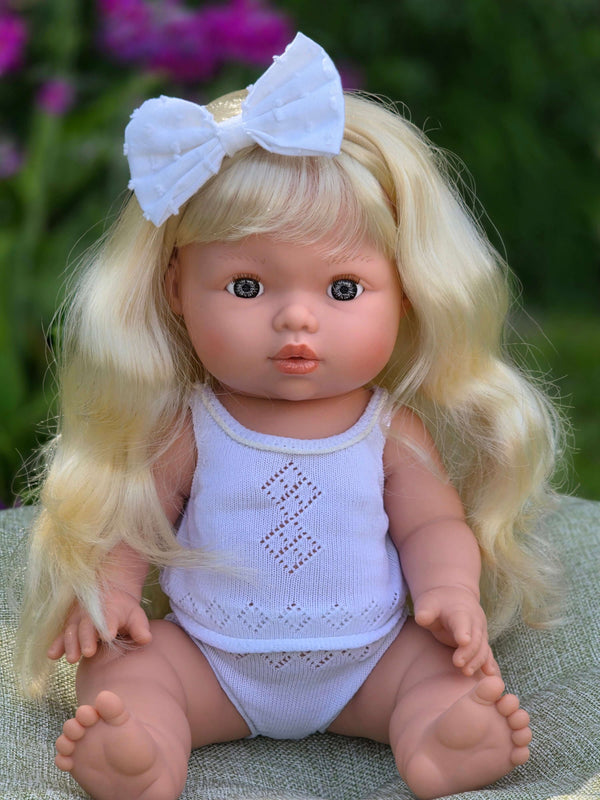 Mini Colettos, Sage (Light Blonde Hair with Blue Eyes) doll with long blonde hair and a bow, sitting outdoors.