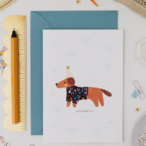 A6 birthday card featuring a sausage dog in a Liberty print coat with 'Let's Party!' text, perfect for celebrating.