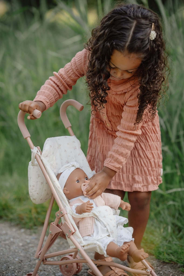 Little Dutch metal doll stroller with a child playing with a doll in a lush outdoor setting.