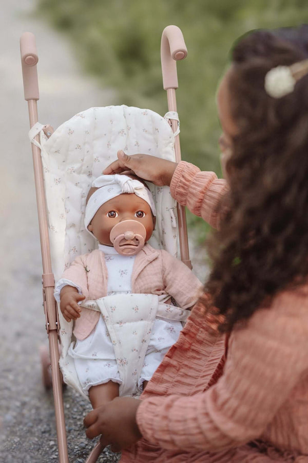 Child playing with a doll in a Little Dutch metal stroller, featuring the White Meadows design, outdoors.