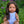 Mini Colettos, Isabel (Hispanic Girl, Brown Straight Hair and Blue Eyes) sitting in grass with flowers.