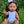 Mini Colettos, Isabel (Hispanic Girl, Brown Straight Hair and Blue Eyes) sitting on grass in a white swimsuit.