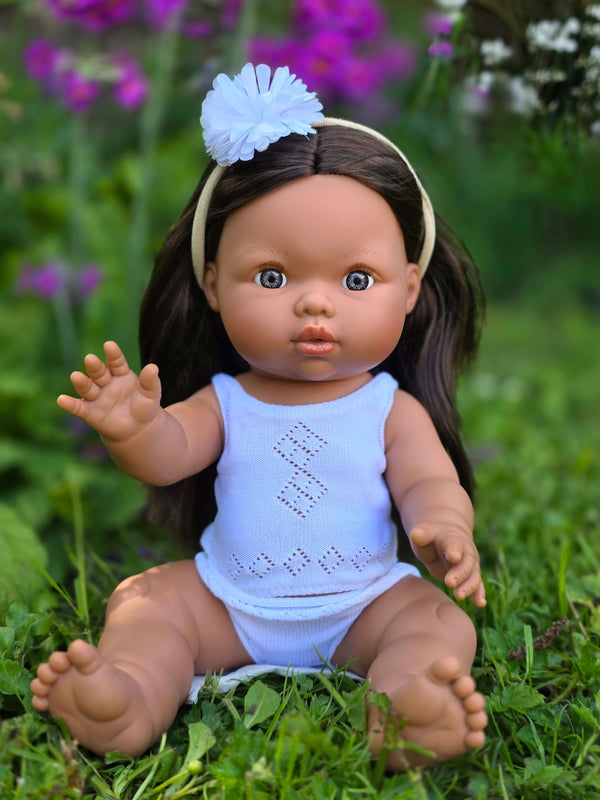 Mini Colettos, Isabel (Hispanic Girl, Brown Straight Hair and Blue Eyes) sitting on grass in a white swimsuit.