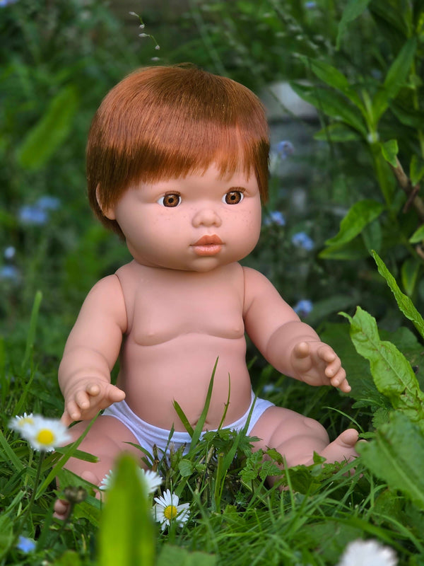 Mini Colettos, Jasper (Boy Doll with Brown Eyes & Red Hair) sitting in grass surrounded by flowers.
