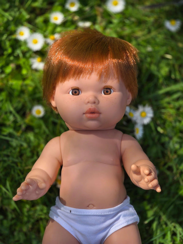 Mini Colettos, Jasper (Boy Doll with Brown Eyes & Red Hair) lying on grass surrounded by flowers.