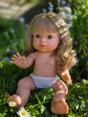 Mini Colettos doll Kate, a blonde-haired girl doll with blue eyes sitting in grass with flowers.