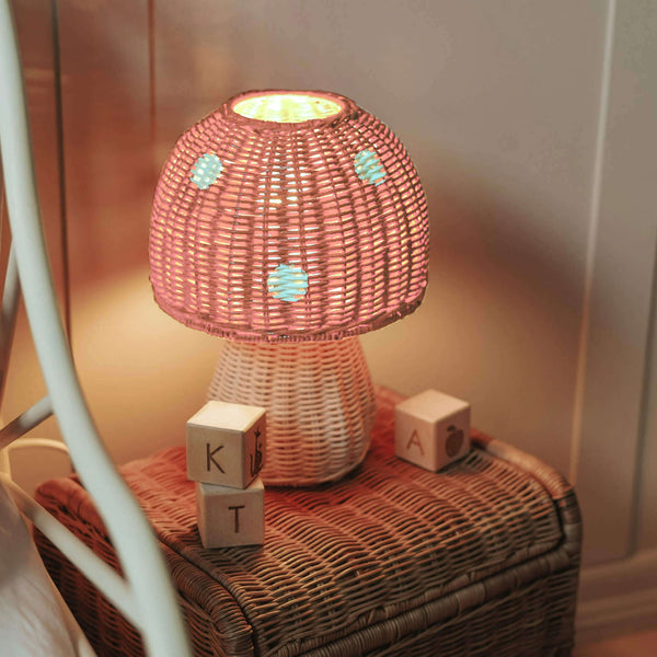 Olli Ella Toadstool Lamp in Musk, a rattan mushroom lamp glowing softly beside wooden blocks.