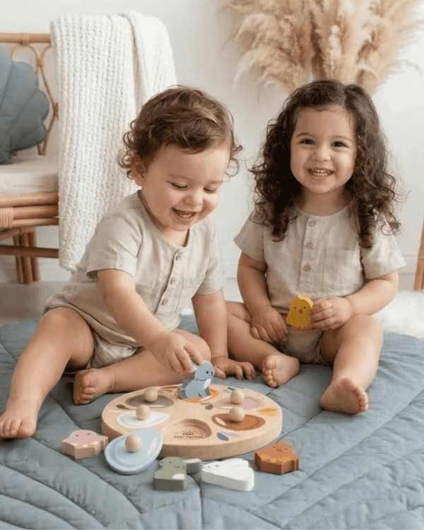 Two toddlers joyfully playing with the Speedy Monkey, Garden Surprise Puzzle, unveiling colorful wooden animals.
