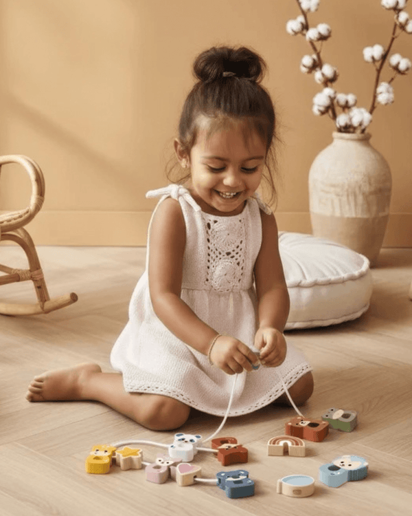 A joyful child playing with Speedy Monkey, Stringable Beads on the floor, enhancing fine motor skills.